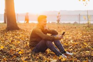 gelukkige kerel die lacht en praat aan de telefoon in het herfstpark foto