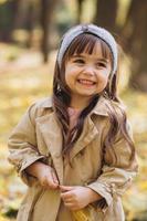 mooi klein meisje in een beige jas loopt in het herfstpark foto
