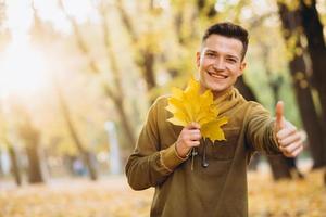 man die lacht en een boeket herfstbladeren vasthoudt in het park foto