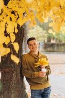 man met een boeket bladeren die koffie drinkt in het herfstpark foto