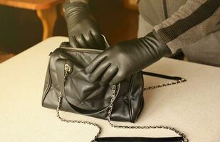rover in zwart kleding en handschoenen zien Aan geopend gestolen Dames tas. een dief evalueert de waarde van gestolen items van een dames handtas in keuken foto