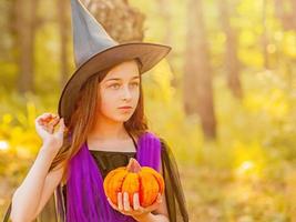 tienermeisje in een halloween-kostuum in het bos met een pompoen