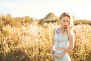 mooi blond vrouw Aan een wandelen in een veld- met droog gras. een wandelen in natuur, zonsondergang in een veld- van pampa gras foto