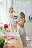 een weinig blond meisje met haar mam Aan een keuken aanrecht versierd met pioenrozen. de concept van de verhouding tussen moeder en dochter. voorjaar atmosfeer. foto