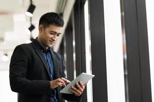 jonge knappe Aziatische zakenman in pak met behulp van tablet op kantoor. foto