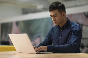 jonge aziatische zakenman die met laptop in bureau werkt.
