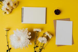 notbook en blanco kaart met bloemen wordt op gele achtergrond geplaatst foto