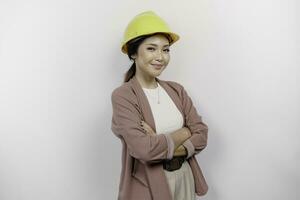 een zelfverzekerd glimlachen Aziatisch vrouw werknemer vervelend veiligheid helm staand met armen gevouwen en op zoek Bij de camera geïsoleerd over- wit achtergrond foto