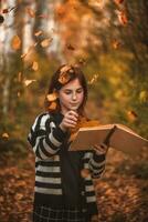 meisje met sproeten met een boek tussen herfst bladeren foto