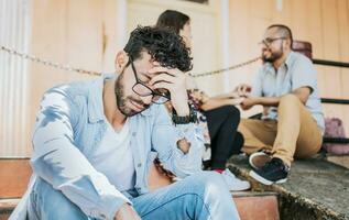 verdrietig vriendje zittend Aan sommige trap terwijl zijn vriendin pratend naar een ander Mens. verdrietig Mens zien zijn vriendin bedrog met zijn vriend. meisje pratend naar een ander Mens en haar vriendje is beledigd foto