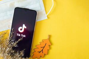 tver, rusland-april 9, 2020, de Tik tok logo Aan een smartphone scherm Aan een geel achtergrond met een medisch masker en droog gras. tik-tok icoon. de Kruis aan tok app. tiktok sociaal netwerk. foto