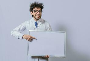 versteld staan Mens in wit jas richten Bij een whiteboard. mannetje wetenschapper in wit jas Holding en richten Bij een blanco whiteboard. slordig haar Mens Holding blanco whiteboard foto