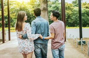 ontrouw meisje wandelen in de park met haar vriendje terwijl Holding een ander Mens hand. liefde driehoek concept. vrouw Holding handen met een ander Mens terwijl wandelen met haar vriendje buitenshuis foto