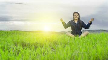 vrouw in de veld- zittend mediteren, vrouw aan het doen yoga in de koel veld- foto