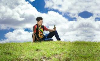 backpacker met telefoon Aan top van een heuvel , een Mens zittend Aan de gras met zijn cel telefoon foto