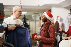 winkelcentrum arbeider tonen kleren naar cliënt, helpen persoon naar Kiezen perfect jasje voor feestelijk Kerstmis diner. Afrikaanse Amerikaans vrouw werknemer aanbevelen kleding voor senior klant. foto