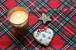 foto brandend kaars in een glas kandelaar en Kerstmis koekjes Aan een rood geruit tafelkleed, top visie