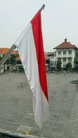 de Indonesisch rood en wit vlag fladdert Aan top van de oud Nederlands erfgoed gebouw. visie van de venster. foto