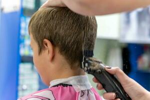 haar- snijdend voor een kind gebruik makend van een haar- tondeuse in een schoonheid salon foto