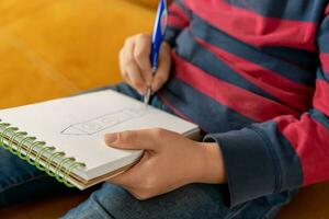 een jongen concentreren Aan tekening in zijn notebook. hij koppelingen de pen in zijn hand- foto