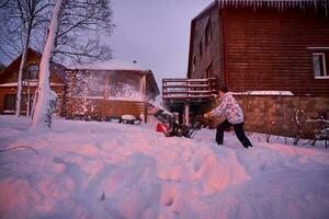 een jong Mens wist sneeuw met een sneeuw blazer in zijn tuin. foto