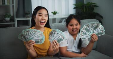 portret van jong Aziatisch vrouw tonen dollar Bij camera en glimlachen Aan sofa in de leven kamer Bij huis. foto