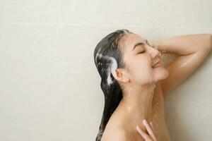 vrouw nemen douche en het wassen haar- met shampoo in badkamer Bij huis foto