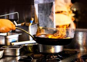 chef-kok koken met vlam in een koekenpan op een keukenfornuis