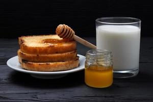 toast op een wit bord, een glas melk en een pot honing foto