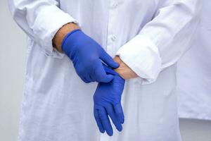 de handen van een dokter in latex handschoenen. de dokter zet Aan steriel handschoenen tegen de achtergrond van een medisch gewaad. foto