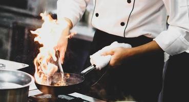 chef-kok koken met vlam in een koekenpan op een keukenfornuis foto