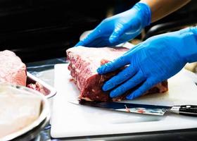 chef-kok snijdt rauw vlees met een mes op een bord, kok snijdt rauw vlees foto