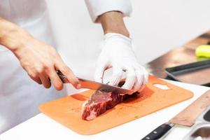 chef-kok die vers rauw vlees snijdt met mes in de keuken foto