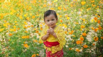 weinig schattig meisje vervelend geel balinees jurk spelen in geel en wit bloem tuin foto