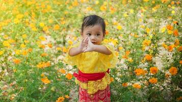 weinig schattig meisje vervelend geel balinees jurk spelen in geel en wit bloem tuin foto
