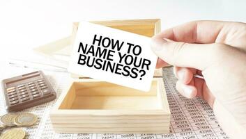 zakenman houden wit kaart met tekst hoe naar naam uw zaken rekenmachine, hout doos, geld en financieel documenten foto
