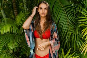 mooi vrouw model- in rood zwemmen slijtage met lang Rechtdoor haar- poseren in tropisch natuur. perfect bruinen lichaam. foto