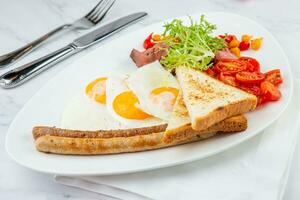 door elkaar gegooid eieren met groenten, kers tomaten, brood, kruiden en worstjes Aan een wit bord kant visie foto