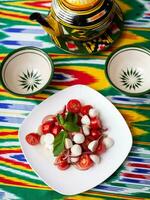 caprese salade met Mazzarella tomaten en kruiden in oosters stijl Aan een tafel met een theepot en een kop voor thee. foto