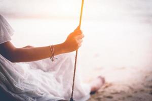 hand van aziatische vrouw op witte jurk zittend op de schommel op het strand foto