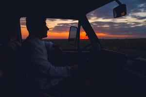 silhouet van de mens die een auto bestuurt op zonsondergangachtergrond foto