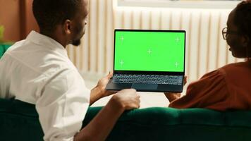 verveeld toeristen aan het kijken video Aan laptop chroma sleutel groen scherm bespotten omhoog aan het wachten voor controleren in werkwijze naar worden over. gasten zittend in hotel foyer terwijl portier werknemer draagt bagage naar hun kamer foto