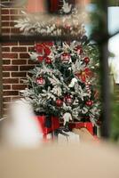 kunstmatig Kerstmis boom versierd met rood kerstballen achter venster in steen muur kantoor. feestelijk groenblijvend met ornamenten gedurende nieuw jaar winter vakantie seizoen in zakelijke werkplaats foto