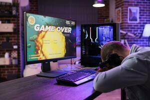 gamer gevoel gestript na verliezende een speler actie videogame niveau, wezen te slim af door vijanden. gebruiken Mens plaatsen hoofd Aan bureau in frustratie na zien spel over- scherm foto