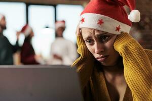 verdrietig ongelukkig Kaukasisch vrouw vervelend de kerstman hoed werken Aan laptop in kantoor Bij Kerstmis vakantie vooravond. uitgeput bedrijf werknemer oplossen taak Aan computer gedurende nieuw jaar seizoen foto