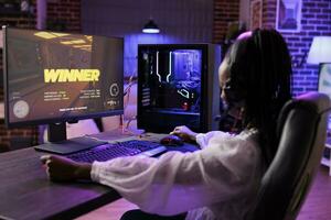 gamer gevoel opgelucht na Tenslotte winnend laatste ruimteschip videogame missie, verslaan laatste baas schurk. Afrikaanse Amerikaans vrouw spelen Aan elektronisch gaming systeem in neon lichten sieren huis foto