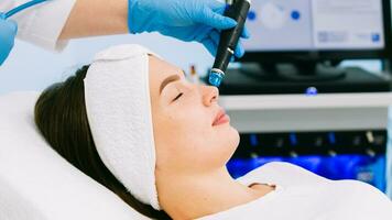 schoonheidsspecialiste kliniek. professioneel vrouw schoonheidsspecialist aan het doen hydrafaciale procedure terwijl wezen een werk. aantrekkelijk mooi hoor vrouw aan het liegen Aan de medisch bed terwijl hebben schoonheid procedures foto