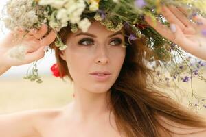 mooi vrouw met een krans Aan haar hoofd zittend in een veld- in bloemen foto