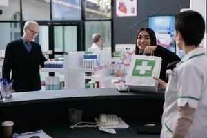 apotheek Kassa geven cliënt boodschappen doen zak met geneeskunde Bij uitchecken. glimlachen casian vrouw nemen aankoop pakket van farmaceutisch werknemer Bij medisch kleinhandel op te slaan teller bureau foto