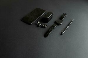 zwart pen, zwart slim horloge, smartphone, draadloze hoofdtelefoons Aan donker achtergrond foto